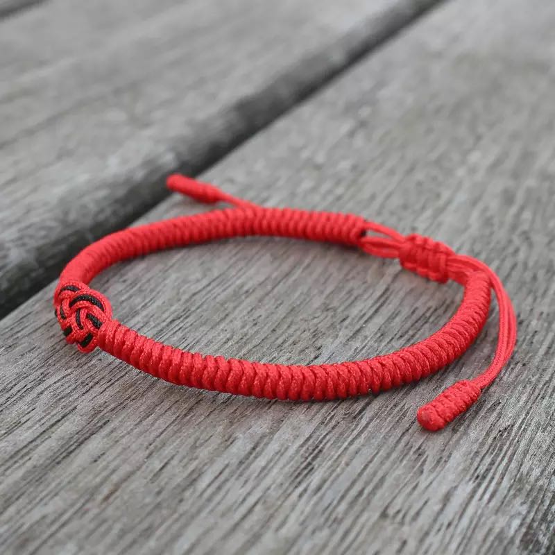 Bracelet tibétain fil rouge tressé avec un nœud central noir, symbole de protection et de chance, posé sur des planches de bois