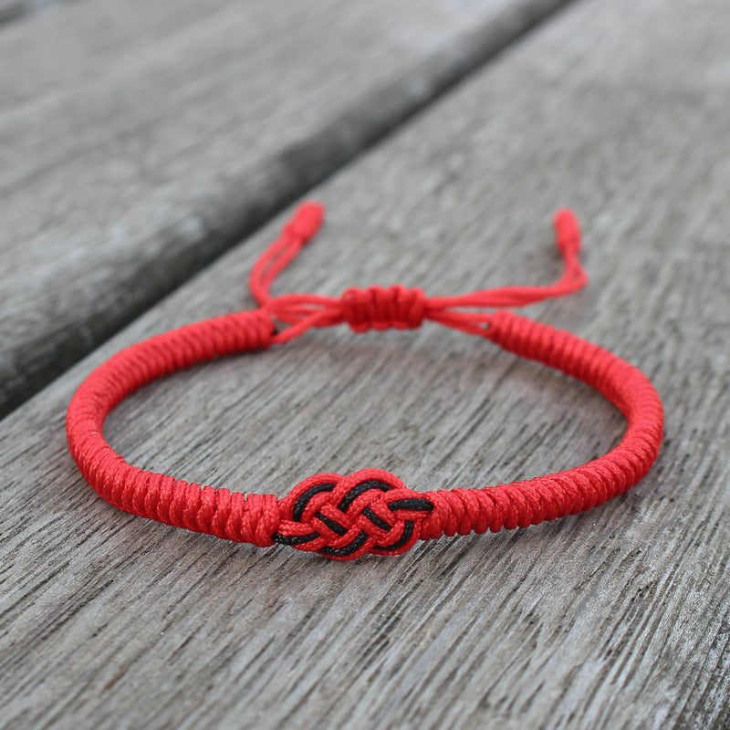 Bracelet fil rouge avec un nœud celtique noir au centre, réglable, sur fond de bois