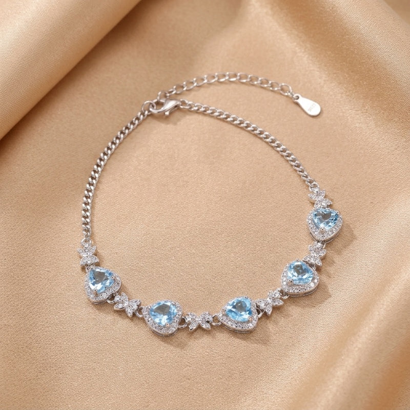 Bracelet en argent 925 orné de cinq pierres bleues en forme de cœur, serties de zirconium, disposées en arc sur une chaîne maille forçat.