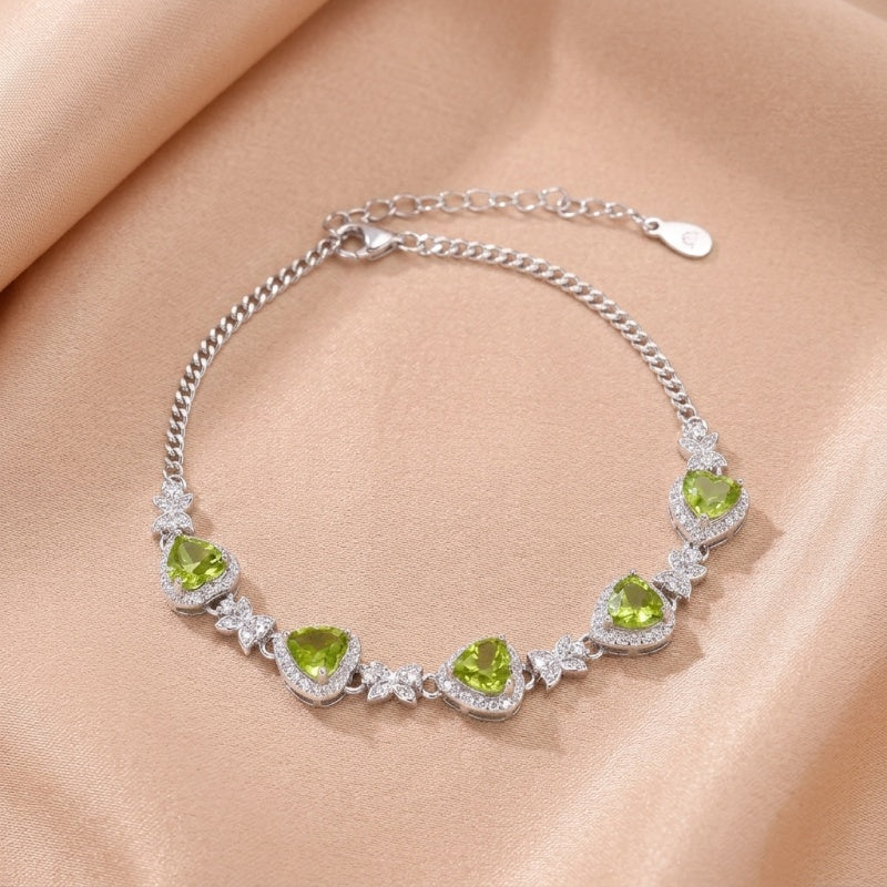 Bracelet en argent avec des pierres vertes en forme de cœur serties de diamants blancs et des détails floraux.