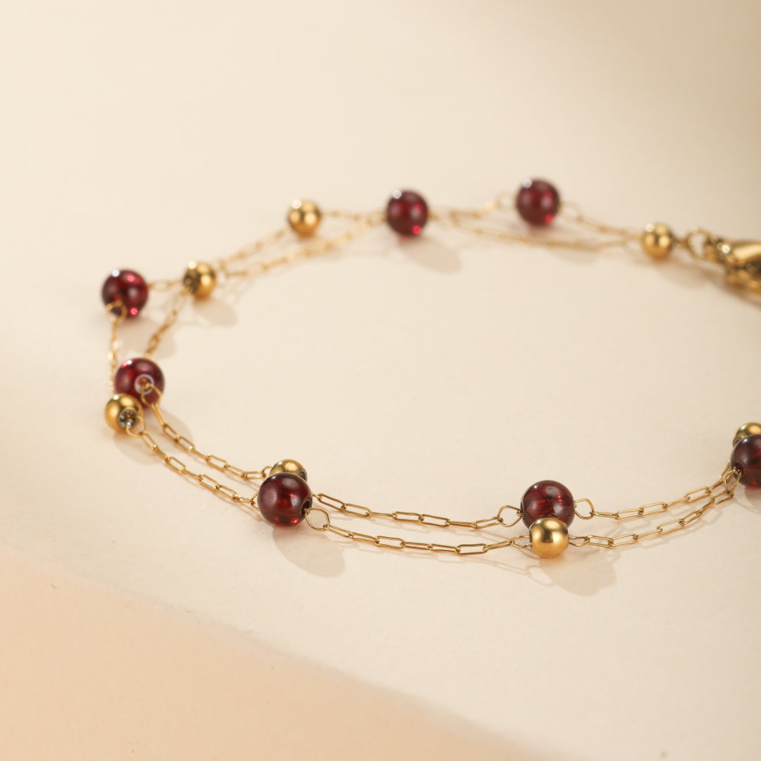 Bracelet fin en plaqué or 18K avec des perles rondes de grenat rouge profond et des petites perles dorées, monté sur deux chaînes délicates.
