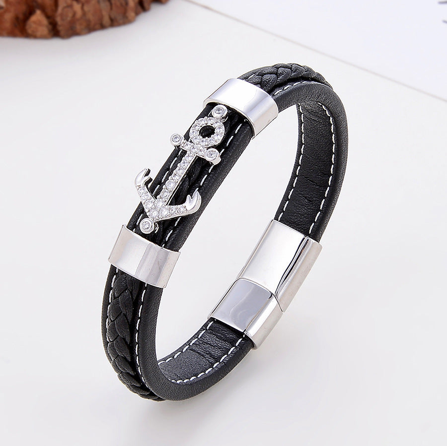 Bracelet pour homme en cuir noir tressé et lisse, orné d'une ancre scintillante sertie de strass et de détails argentés. Fermoir magnétique argenté.