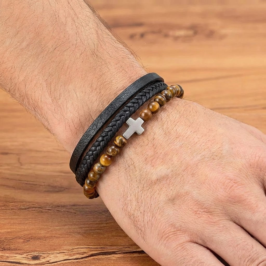 Bracelet homme composé d'un bracelet en cuir tressé noir, d'un bracelet en cuir lisse noir et d'un bracelet de perles œil de tigre orné d'une croix argentée.