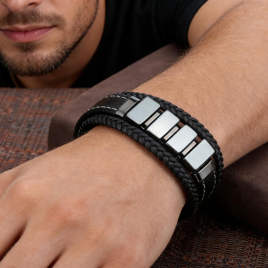Bracelet homme cuir tressé noir avec des inserts rectangulaires en hématite argentée, coutures blanches contrastantes, porté au poignet.