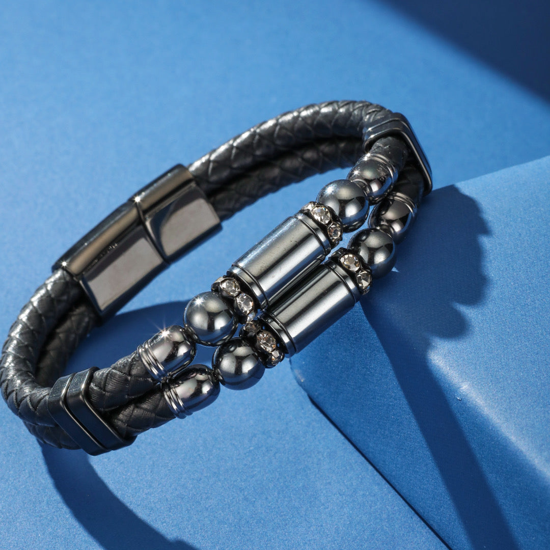 Bracelet homme double rang en cuir tressé gris orné de perles rondes en hématite et de cylindres métalliques sertis de cristaux brillants, avec fermoir magnétique.