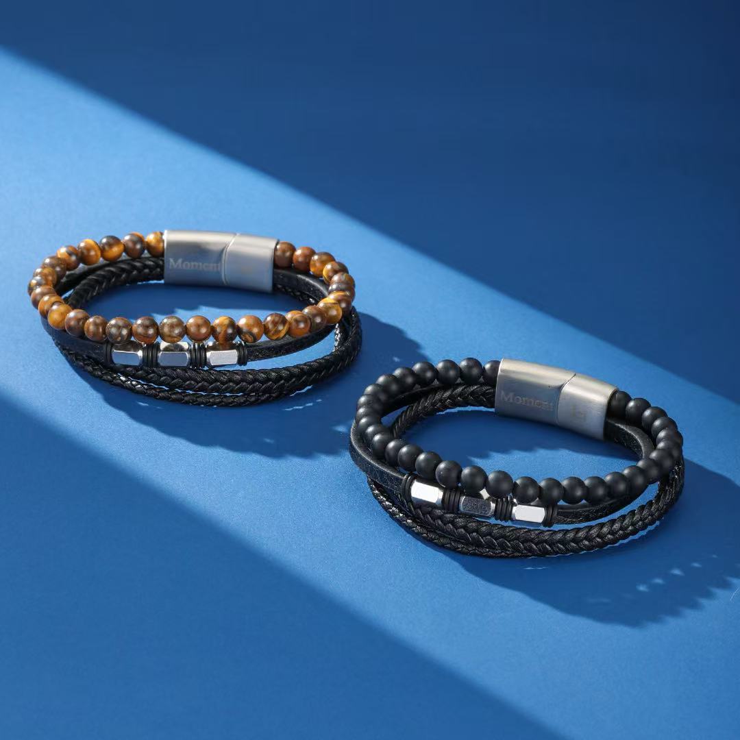 Deux bracelets masculins en cuir tressé noir, l'un avec des perles œil de tigre et l'autre avec des perles d'onyx, ornés d'accents argentés et d'un fermoir magnétique.
