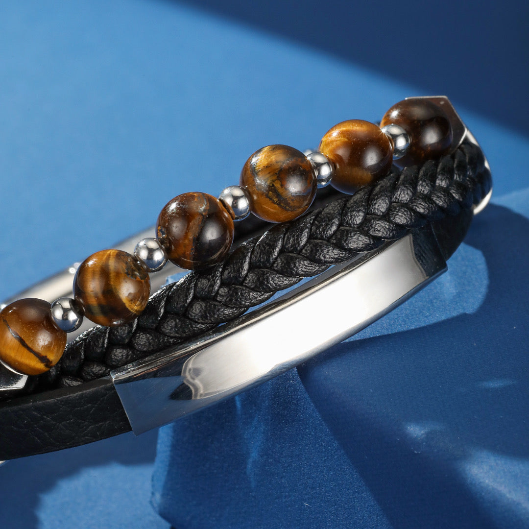 Bracelet pour homme en cuir tressé noir, orné de perles naturelles d'œil de tigre et d'un fermoir métallique argenté, sur fond bleu.