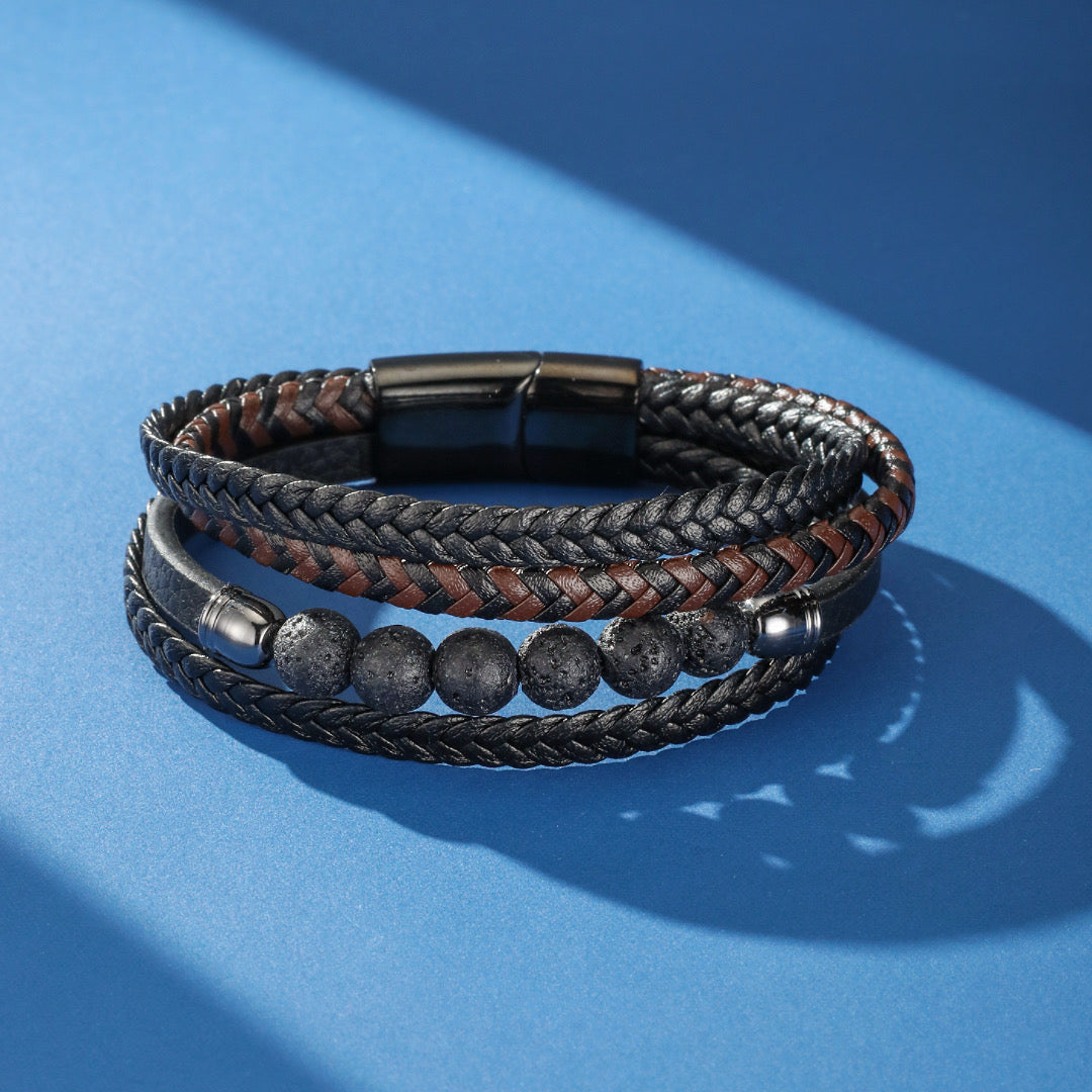 Bracelet homme multicouche en cuir tressé noir et marron, avec des perles de pierre de lave et un fermoir magnétique noir, sur fond bleu.