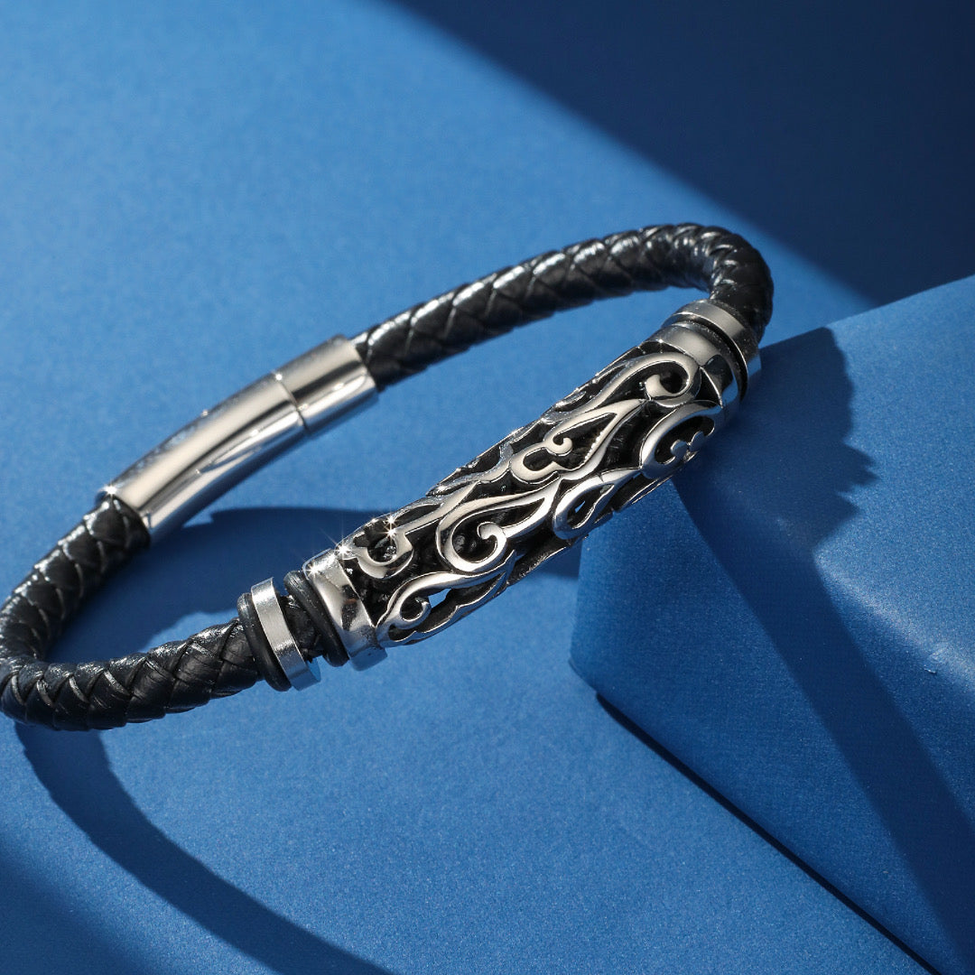 Bracelet homme en cuir tressé noir avec un tube central en acier inoxydable gravé de motifs tribaux et un fermoir magnétique.