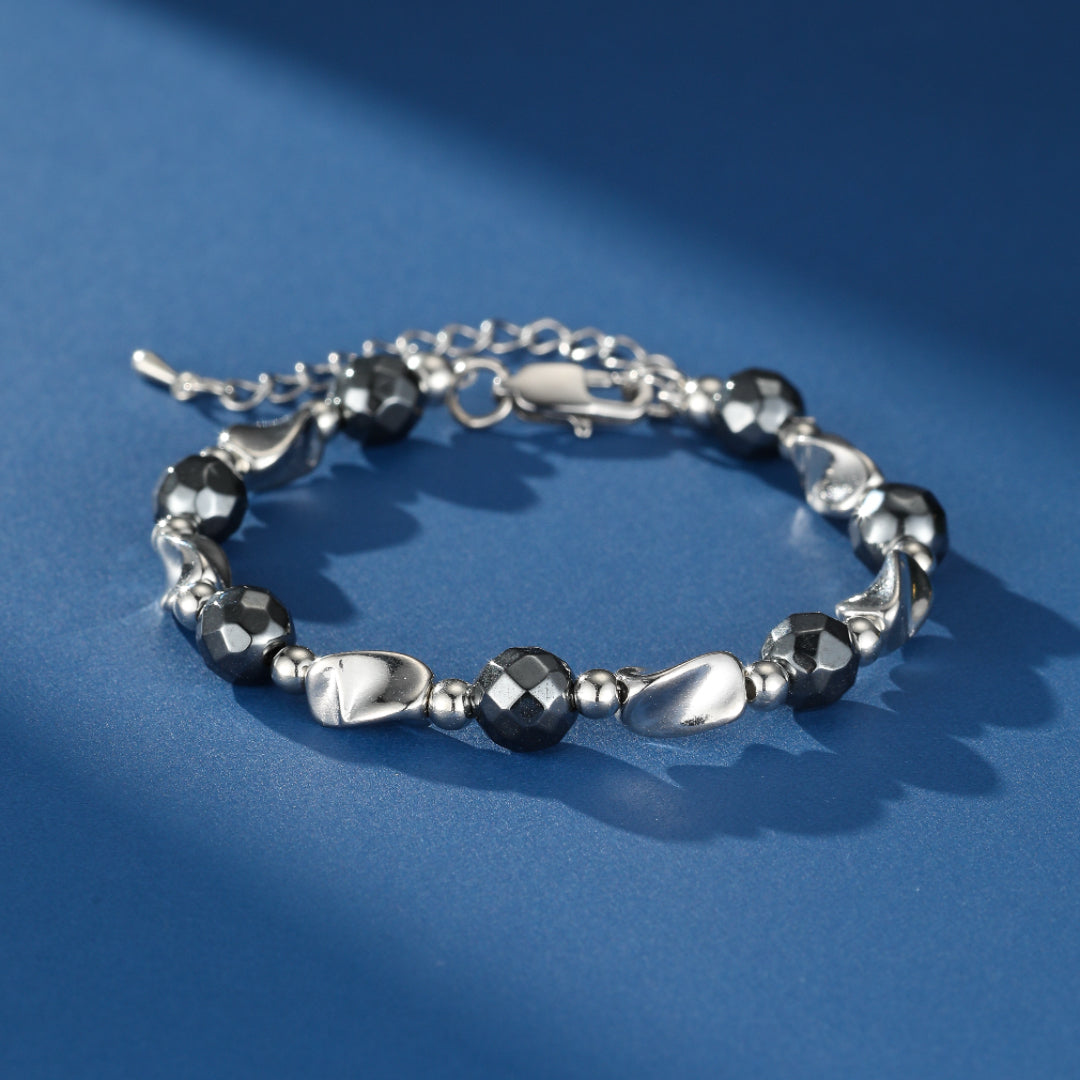 Bracelet pour homme en argent avec des perles d'hématite facettées noires et des éléments argentés polis sur fond bleu.