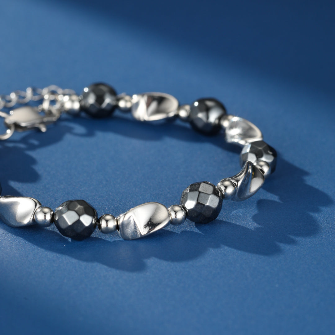 Bracelet pour homme avec des perles d'hématite facetées noires et des éléments lisses en argent sur fond bleu.