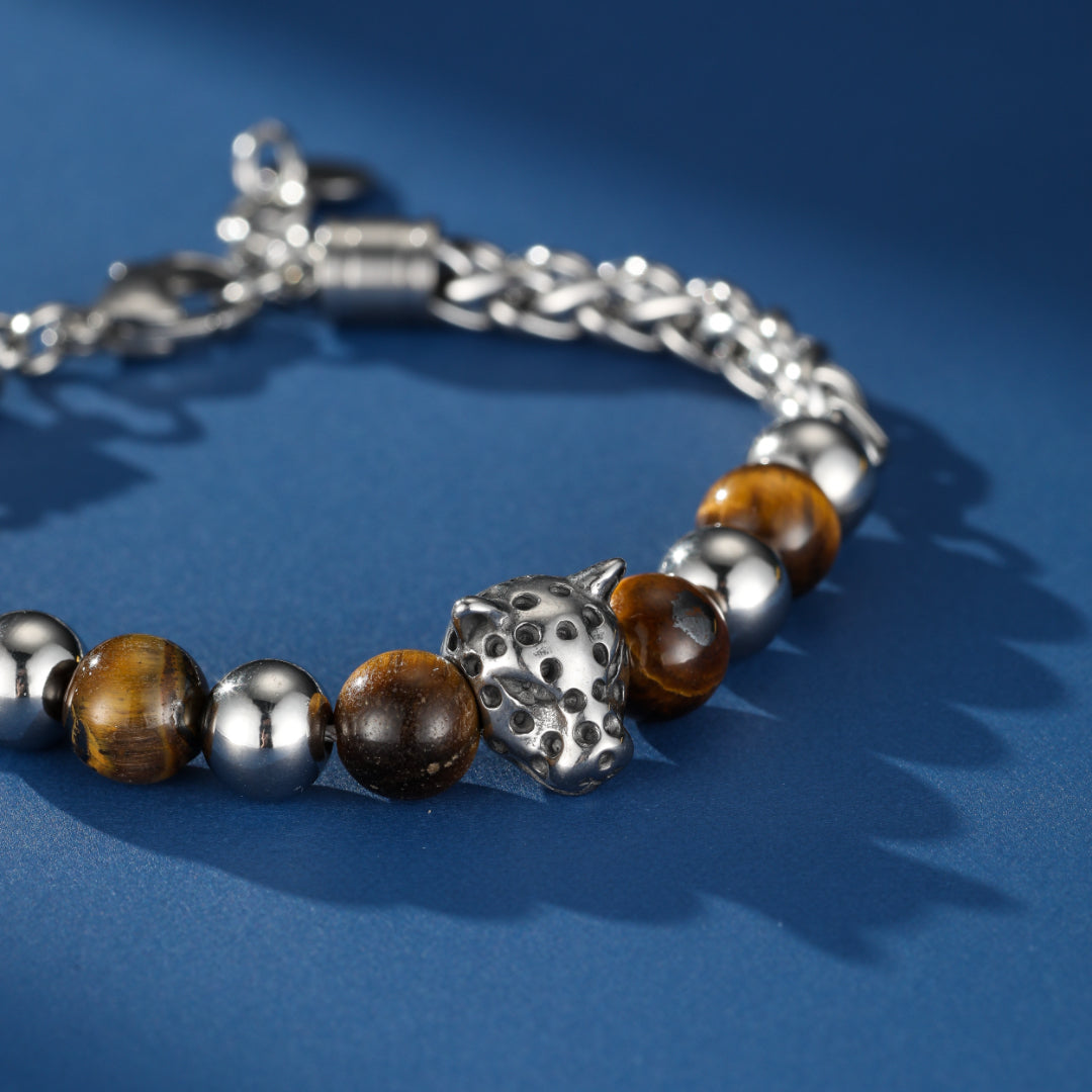 Bracelet homme en œil de tigre et perles argentées avec un pendentif tête de léopard sur fond bleu.