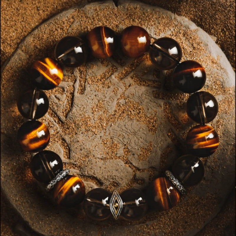 Bracelet pour homme composé de perles d'œil de tigre et de quartz fumé, avec des accents argentés, sur un fond texturé.