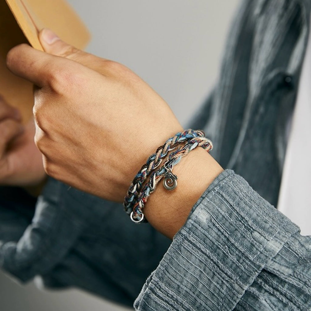 Bracelet tressé multicolore avec un petit pendentif spirale argenté, porté au poignet d'un homme.