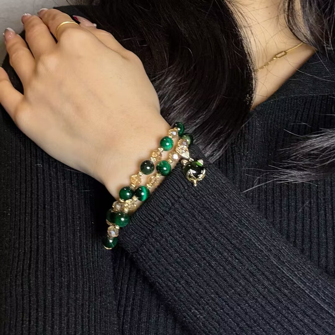 Bracelet double rang avec perles œil de tigre vertes et breloque tête de chat dorée, porté au poignet d'une femme.