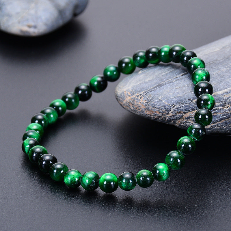 Bracelet en œil de tigre vert avec des perles rondes polies, posé sur une surface sombre à côté de pierres grises.