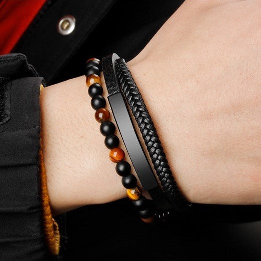 Bracelet en cuir tressé noir et bracelet en perles œil de tigre et onyx mat sur un poignet masculin.