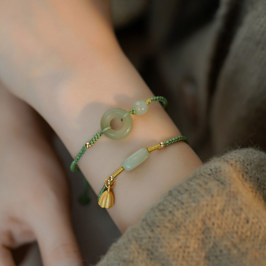 Bracelet en jade vert avec un pendentif en forme de fleur de lotus dorée et un anneau en jade, porté au poignet.