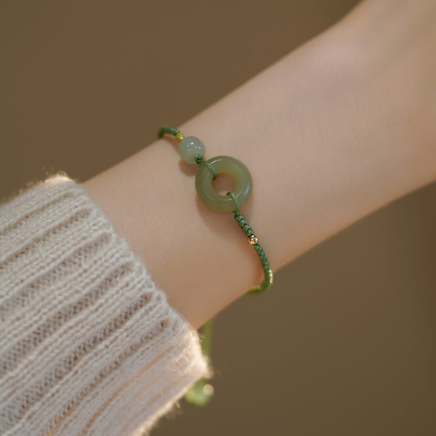 Bracelet en jade vert avec un pendentif rond et une petite perle, porté au poignet sur un pull blanc.