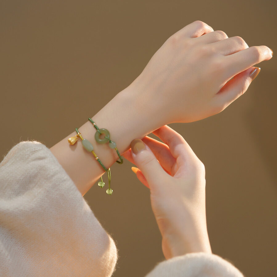 Deux bracelets en jade vert, l'un avec un pendentif en forme de rondelle et l'autre avec des perles allongées et un pendentif en forme de fleur de lotus, portés à un poignet