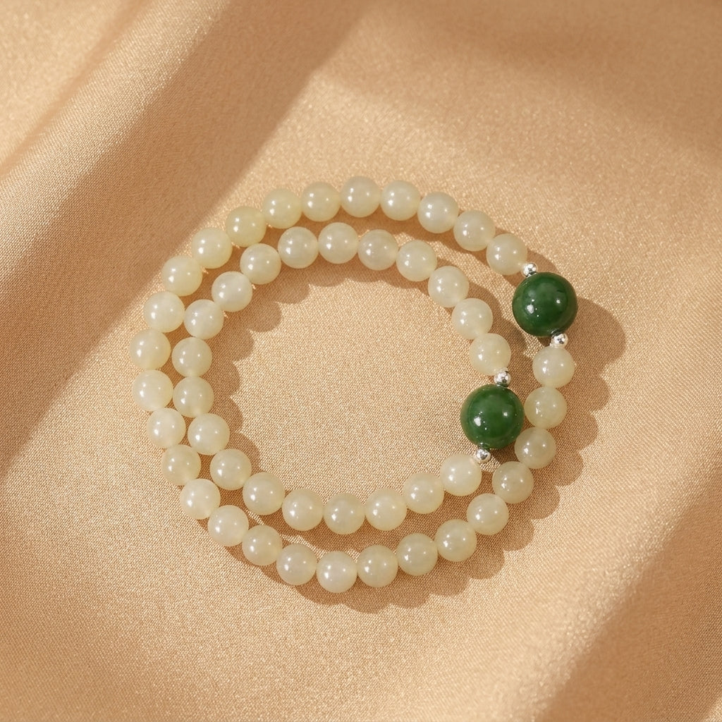 Bracelet double rang en jade néphrite clair et perles vertes, avec des intercalaires en argent, sur fond satiné beige.