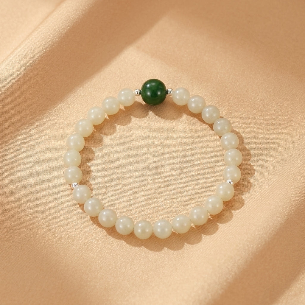 Bracelet en jade néphrite blanc perlé avec une perle de jade vert foncé au centre, monté sur un fil argenté, sur un fond de tissu satiné beige.