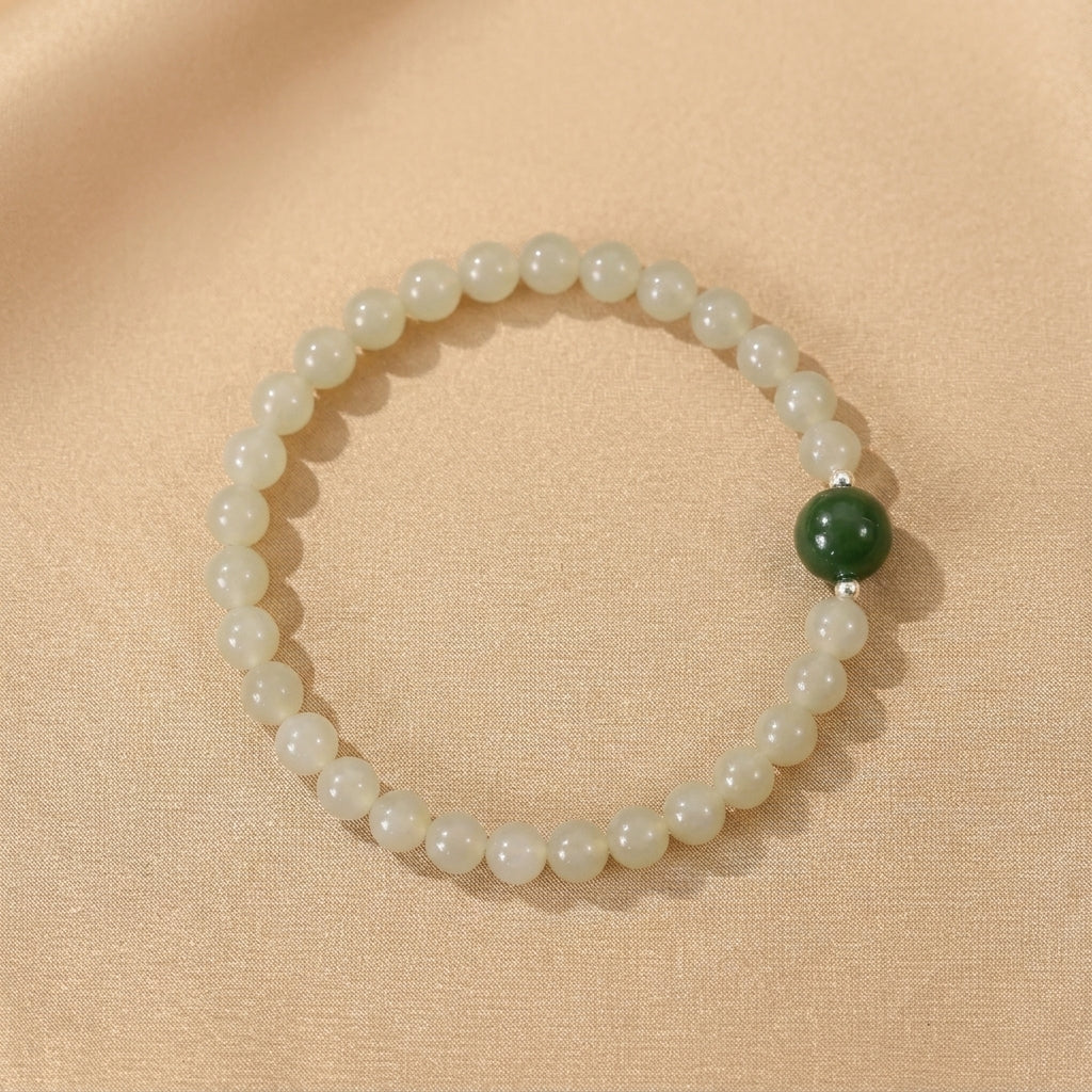 Bracelet en jade néphrite clair avec une perle centrale en jade vert foncé et de petites perles d'argent, sur un fond texturé beige.