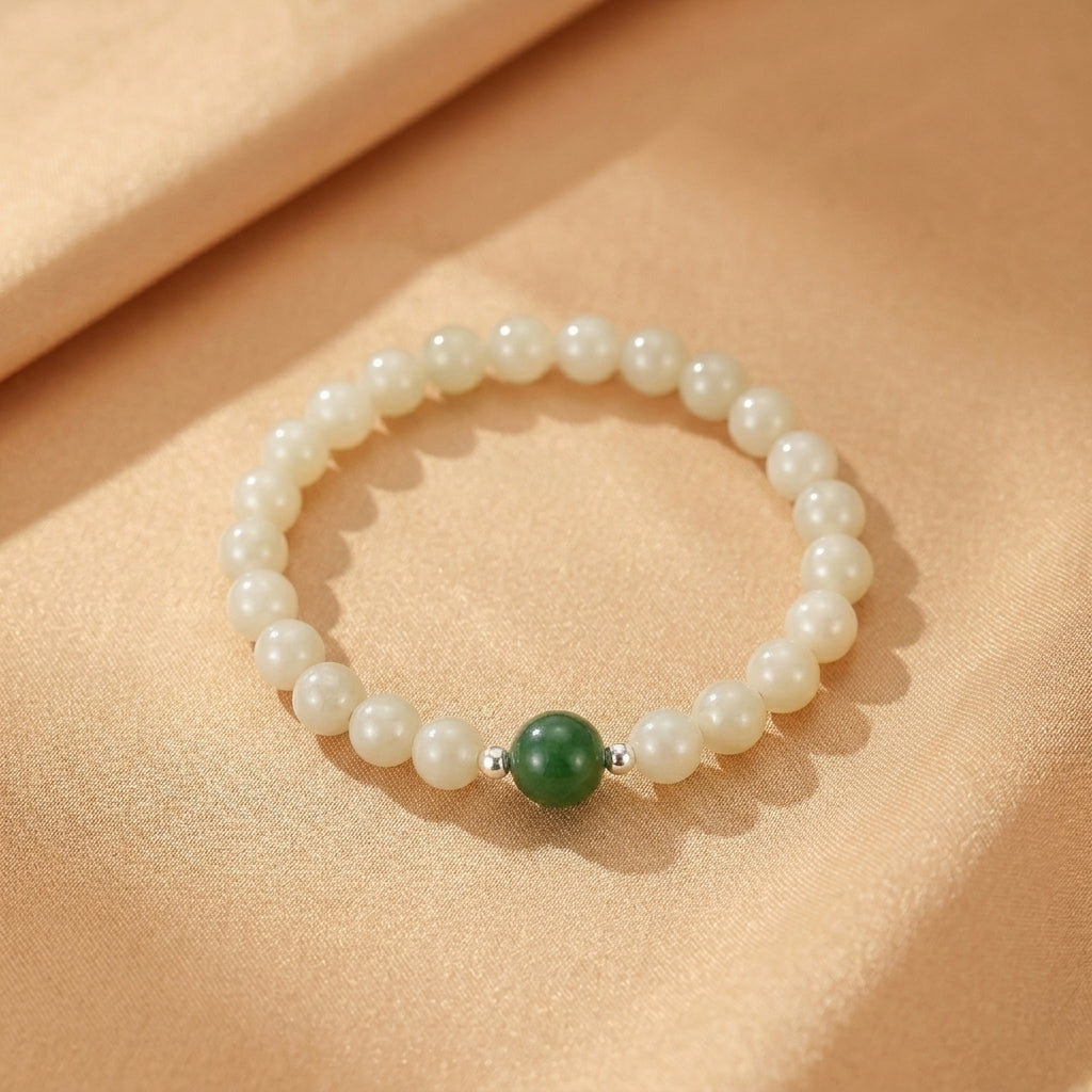 Bracelet en perles de jade néphrite blanc crème et une perle centrale en jade vert profond, avec de petites perles d'argent, sur fond satin beige
