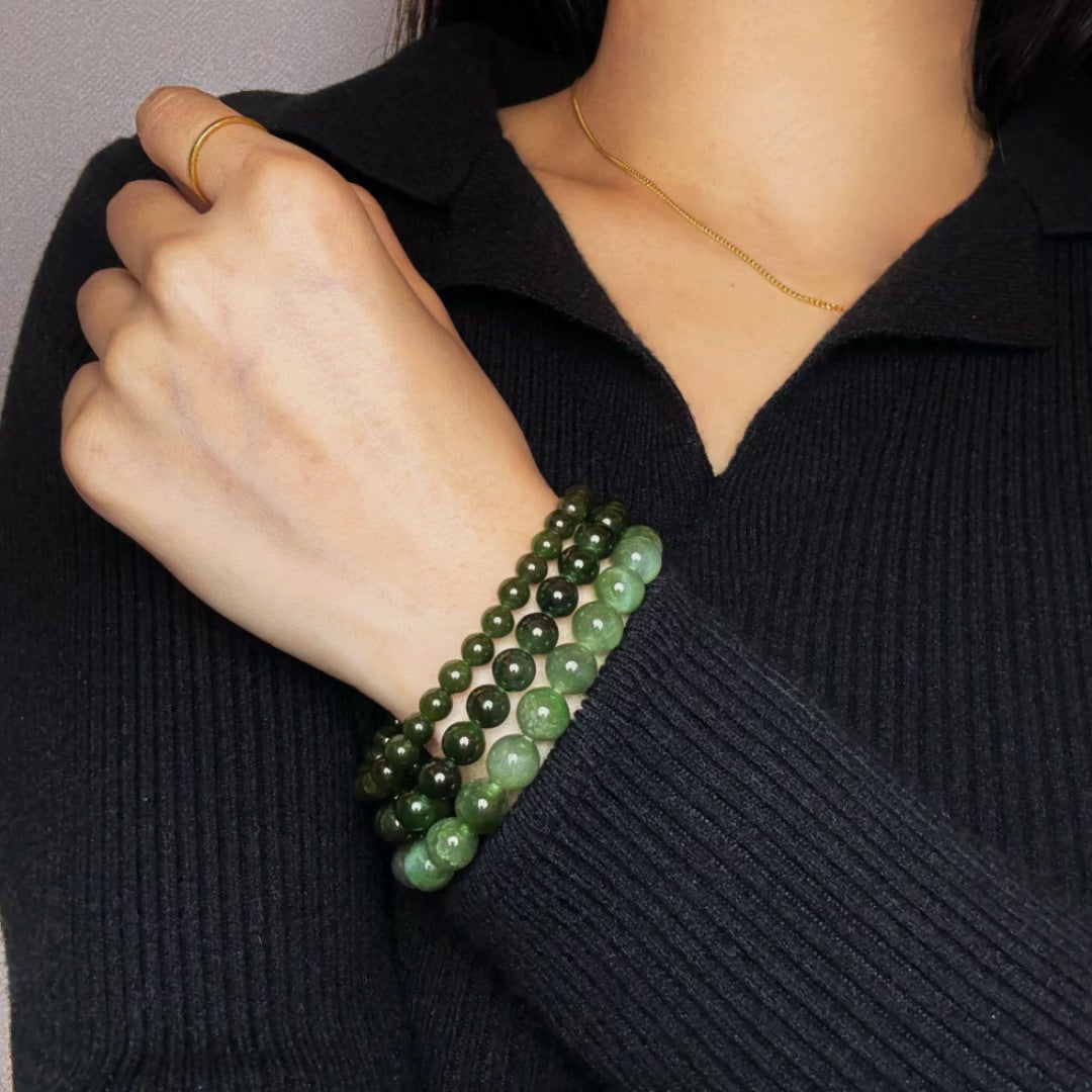 Trois bracelets en perles de jade vert de différentes tailles, portés sur le poignet d'une personne portant un pull noir.