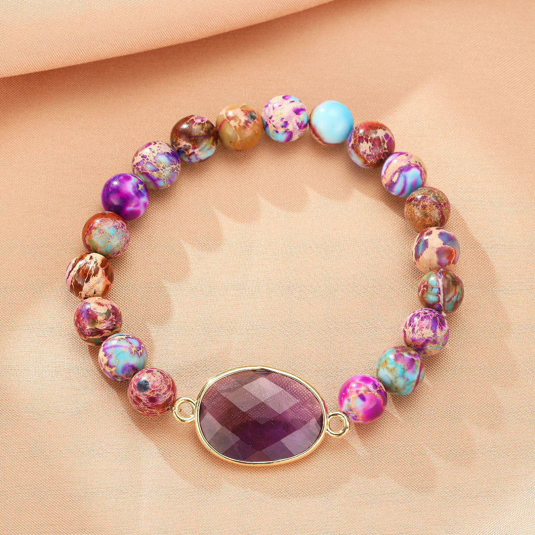 Bracelet élastique "Éveil des Sens" en jaspe multicolore avec une pierre centrale ovale violette facettée sur fond beige rosé.