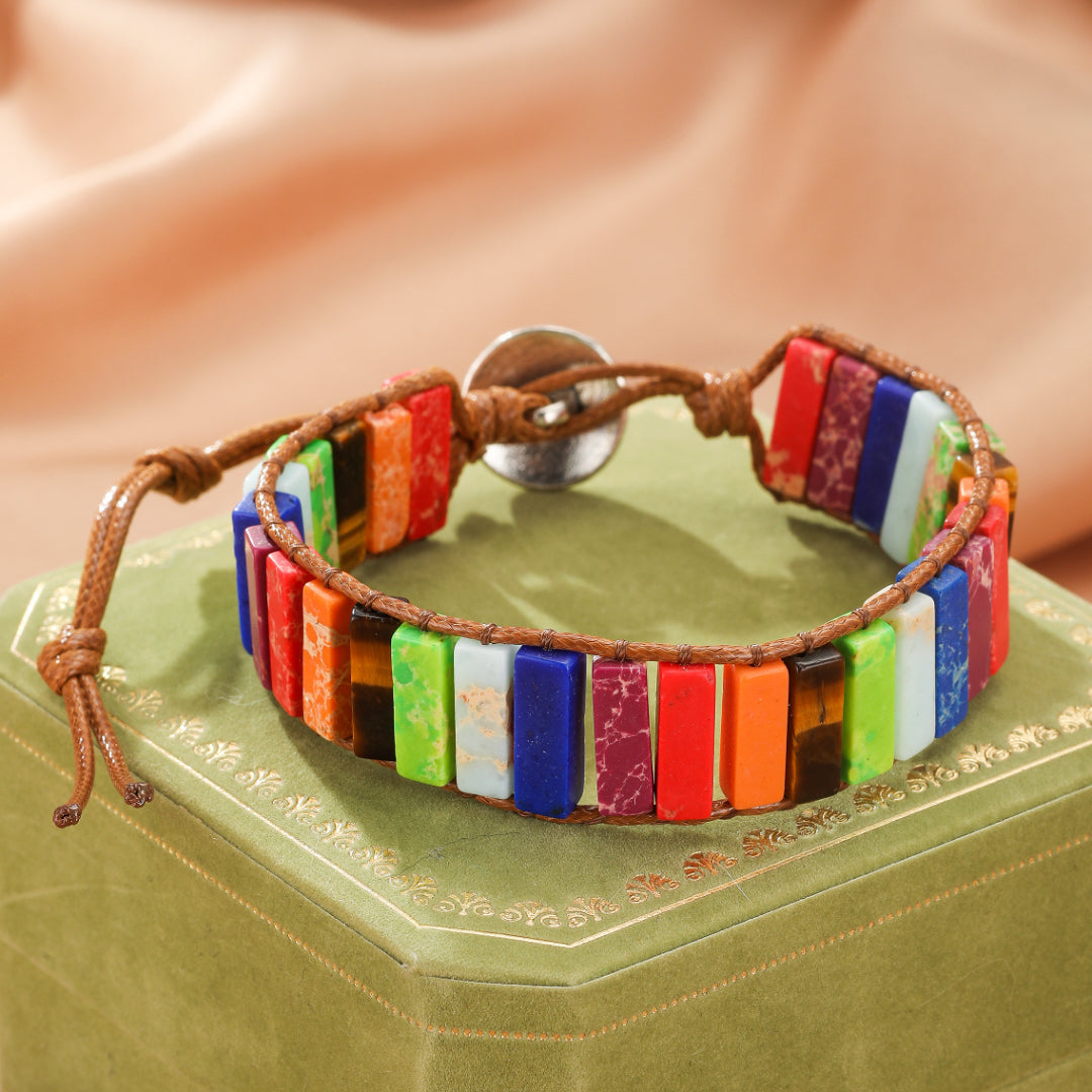 Bracelet en jaspe multicolore avec des pierres rectangulaires assemblées sur un cordon en cuir marron, fermé par un bouton argenté.