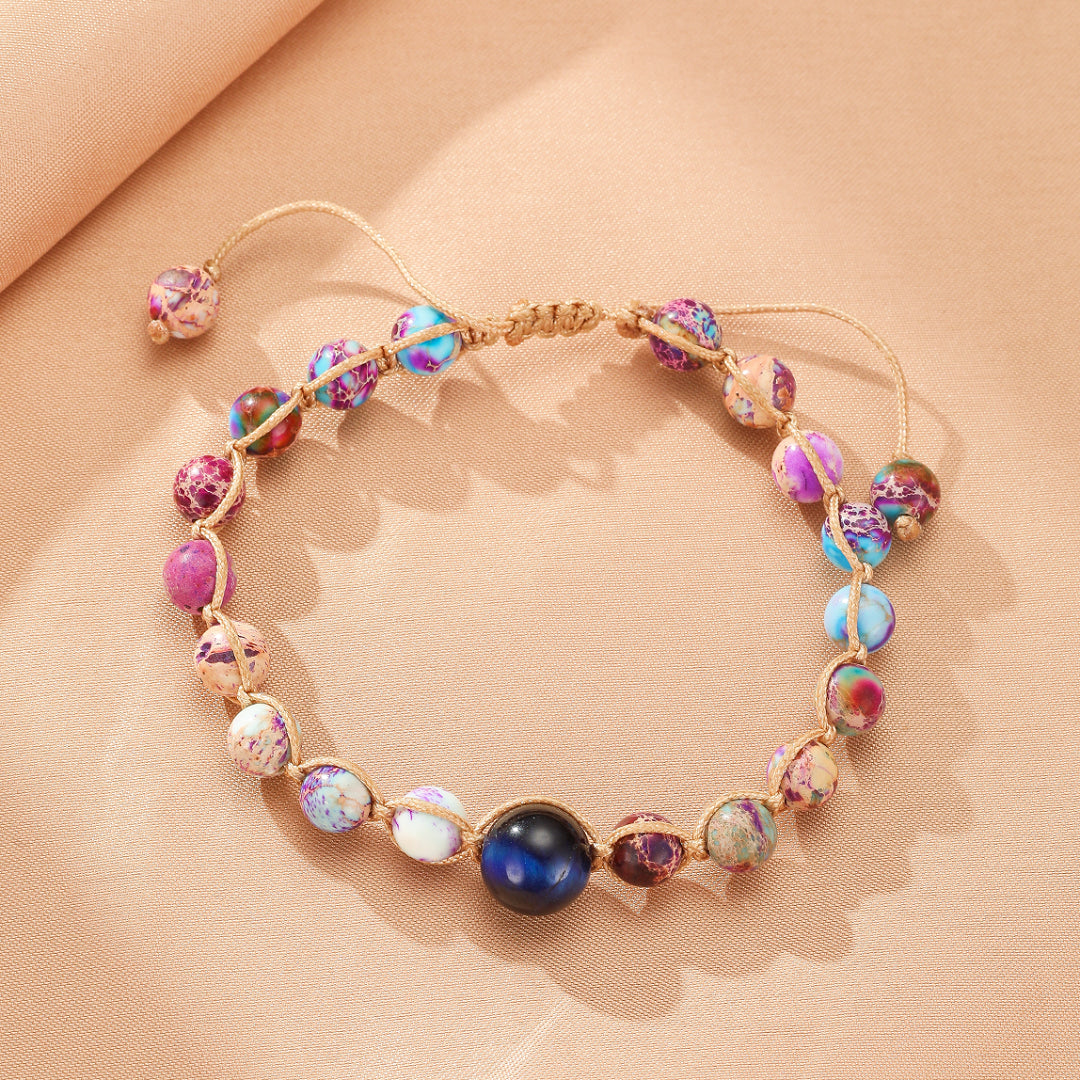 Bracelet ajustable en jaspe impérial multicolore avec une perle centrale bleue foncée, sur fond beige.