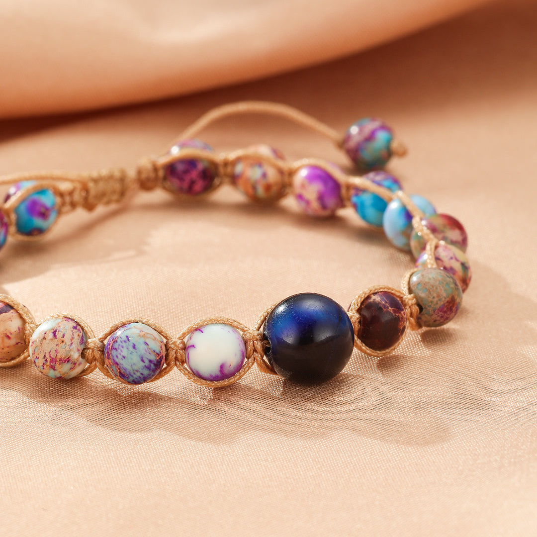 Bracelet fait main avec des perles de jaspe multicolores et une perle bleue centrale, monté sur un cordon en tissu beige.