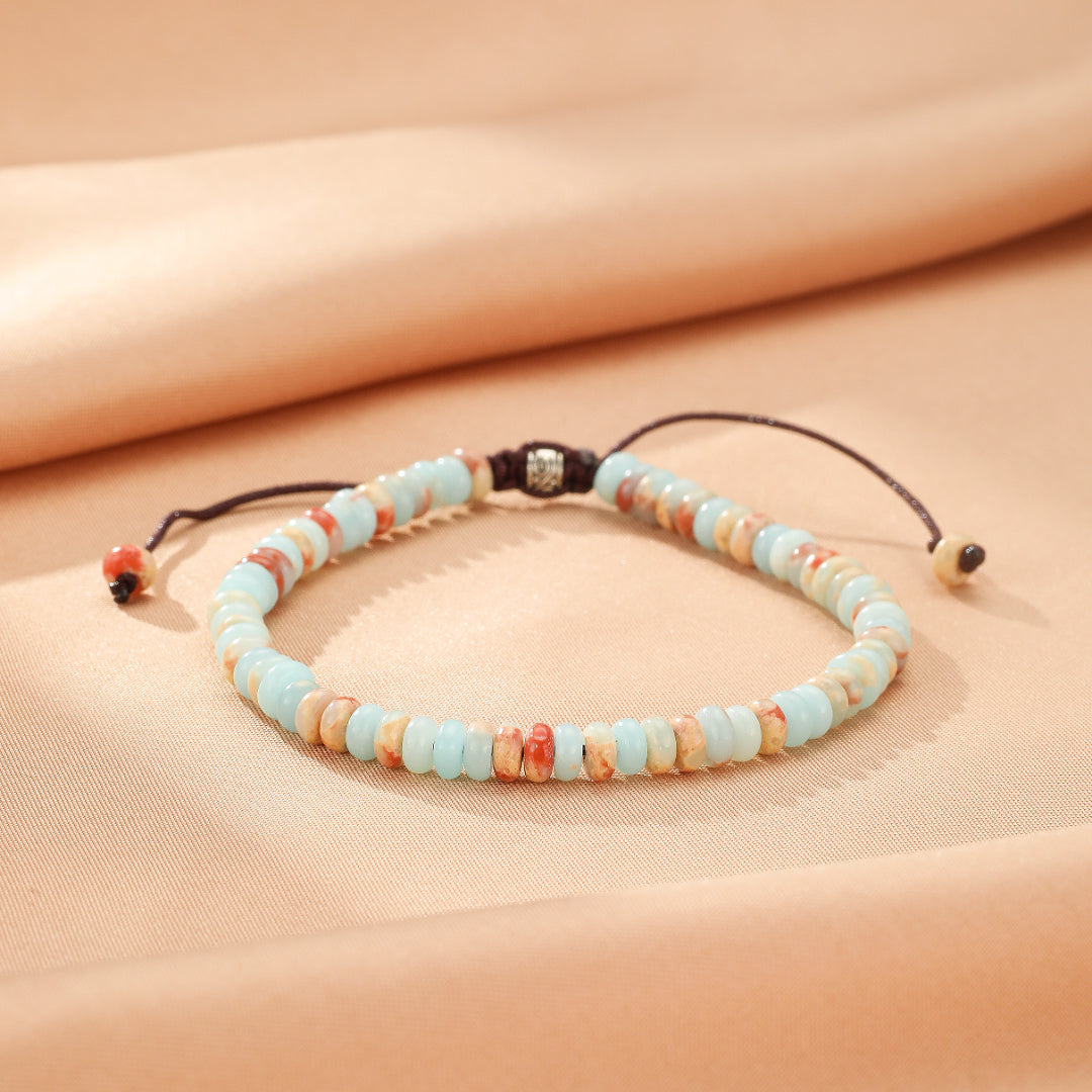 Bracelet en jaspe bleu clair et beige avec des touches de rouge, fermé par un cordon réglable.