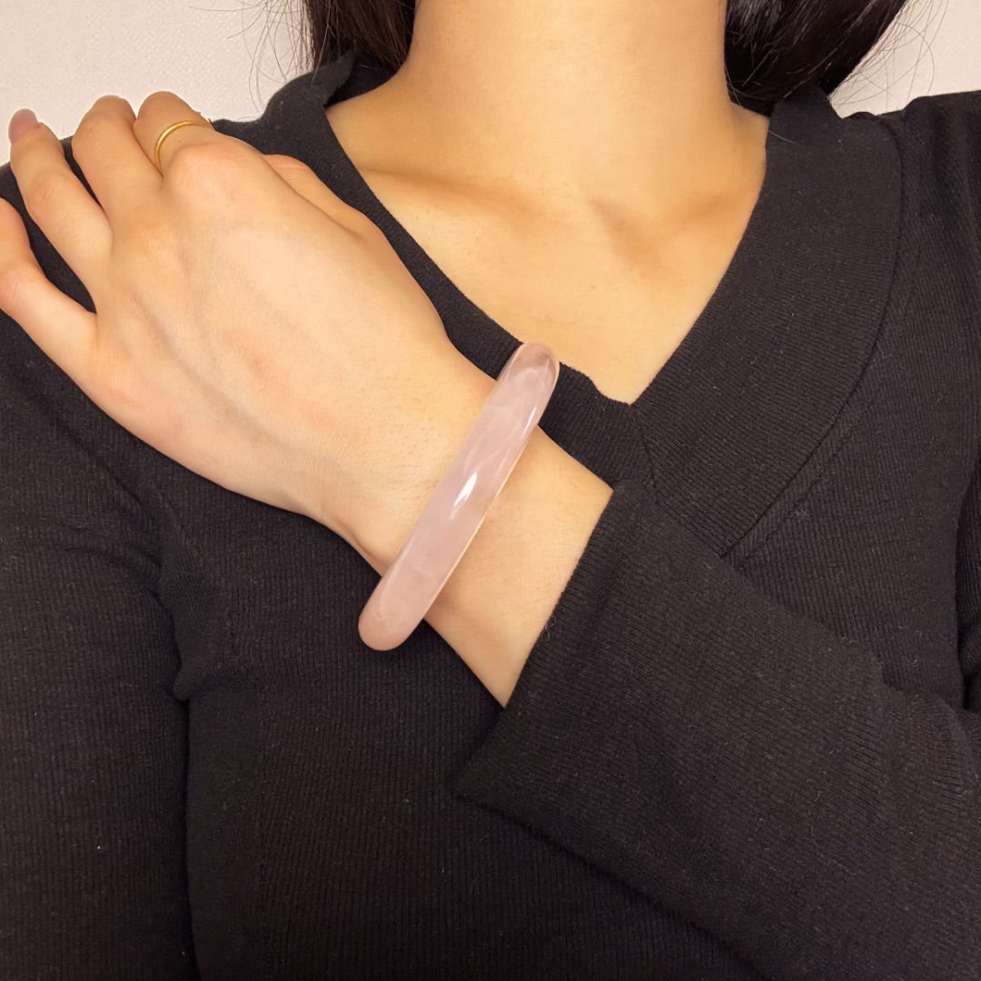 Bracelet jonc en quartz rose naturel translucide, porté au poignet d'une femme sur un haut noir.