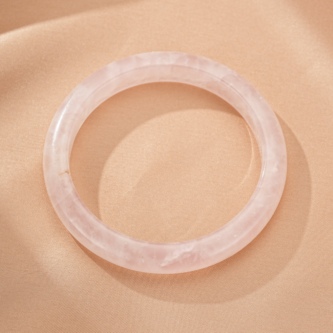 Bracelet jonc en quartz rose naturel, poli et lisse, sur un fond satiné couleur pêche. Ce bijou évoque la douceur et l'amour.