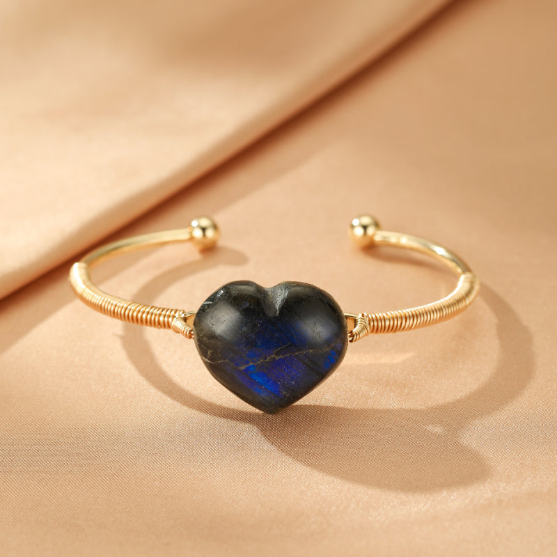 Bracelet jonc ajustable en métal doré, orné d'un pendentif en forme de cœur en pierre de labradorite aux reflets bleus intenses.
