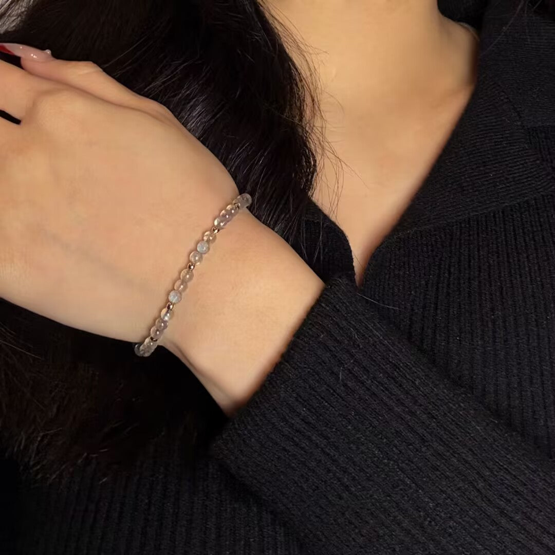 Bracelet fin en pierres de labradorite et perles dorées porté au poignet d'une femme.