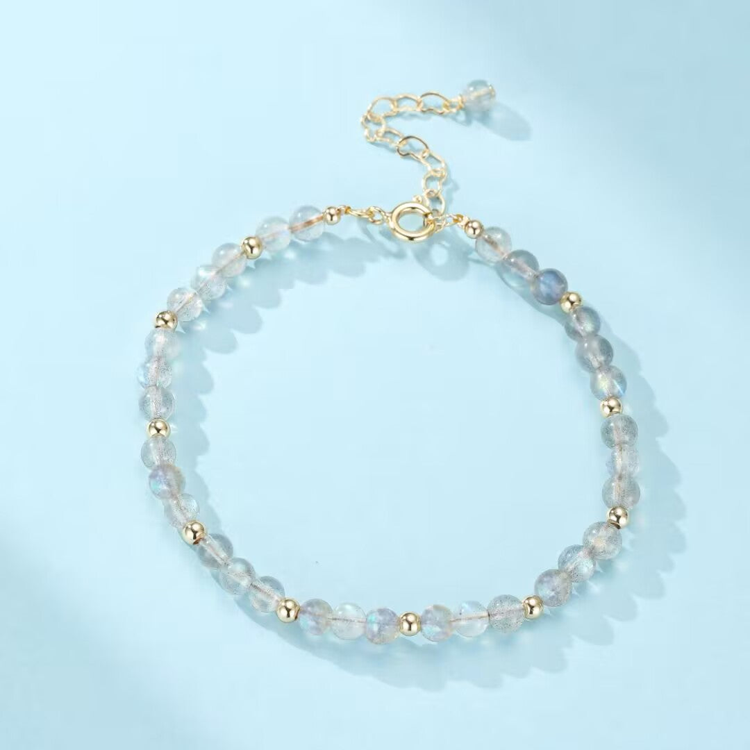 Bracelet délicat en pierres de labradorite et perles dorées, fermoir réglable, sur fond bleu clair