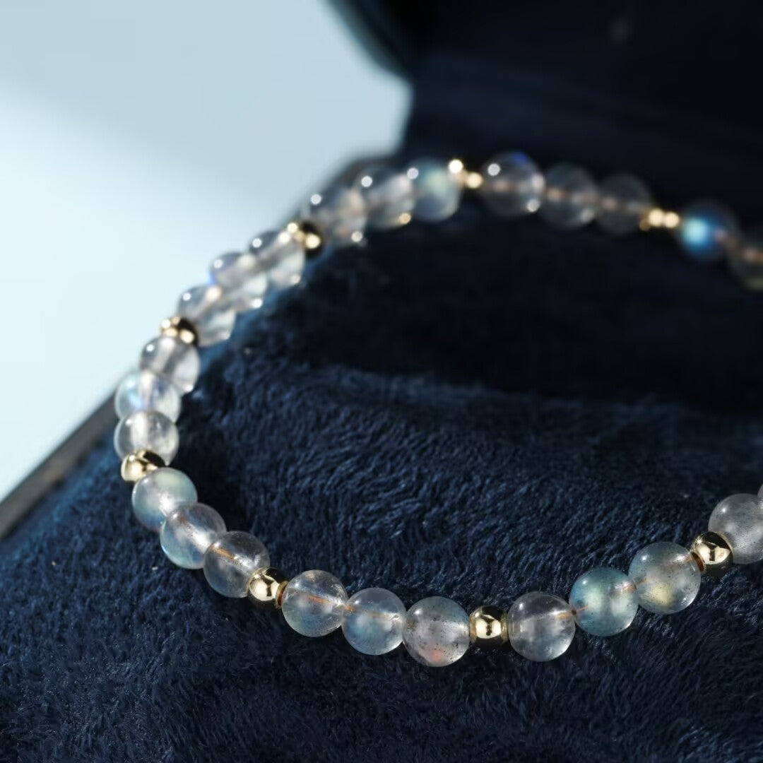 Bracelet fait de perles rondes de labradorite translucide aux reflets bleutés et dorés, montées sur un fil élastique et séparées par de petites perles dorées.