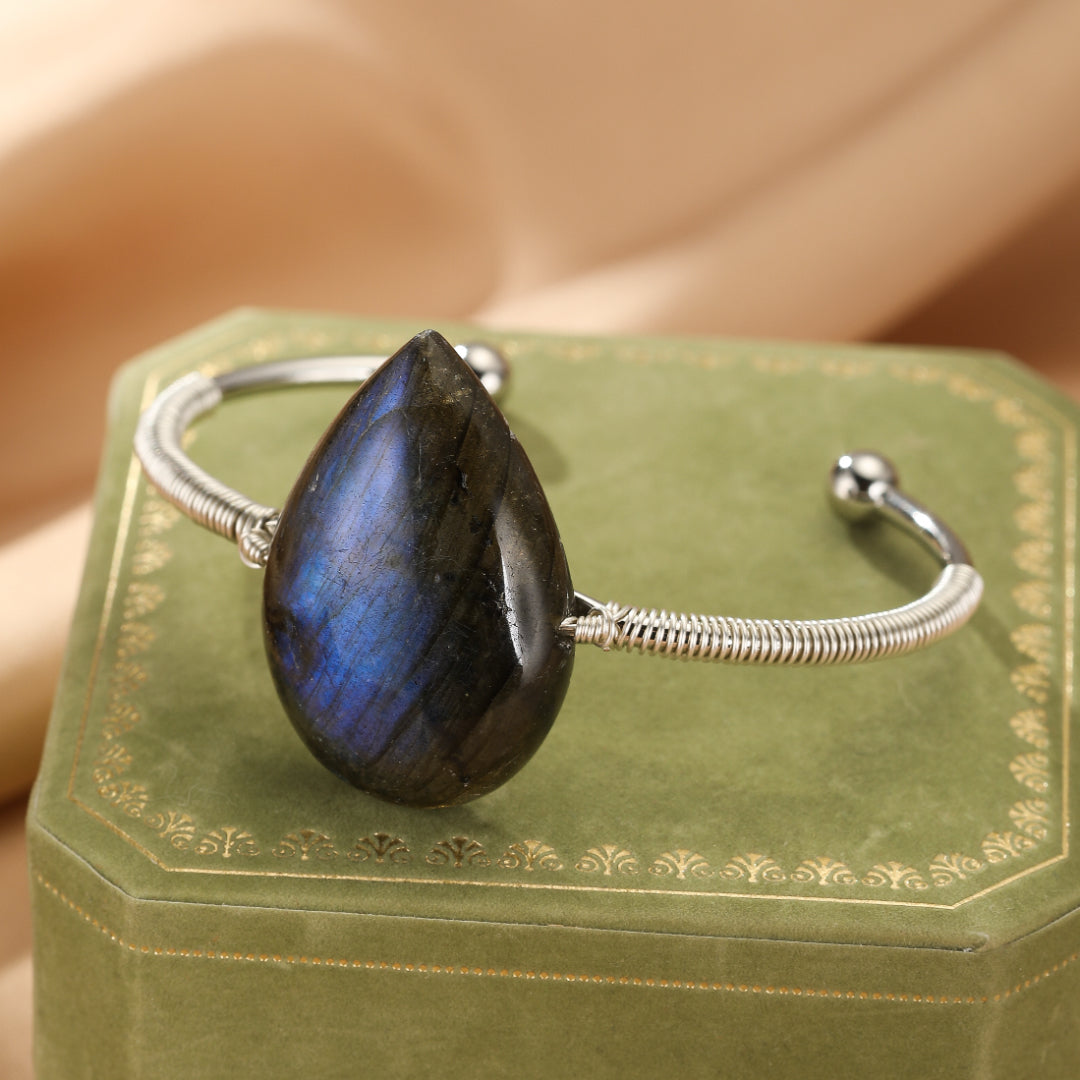 Bracelet jonc argenté orné d'une grosse pierre de labradorite bleue en forme de goutte, posé sur un écrin vert.