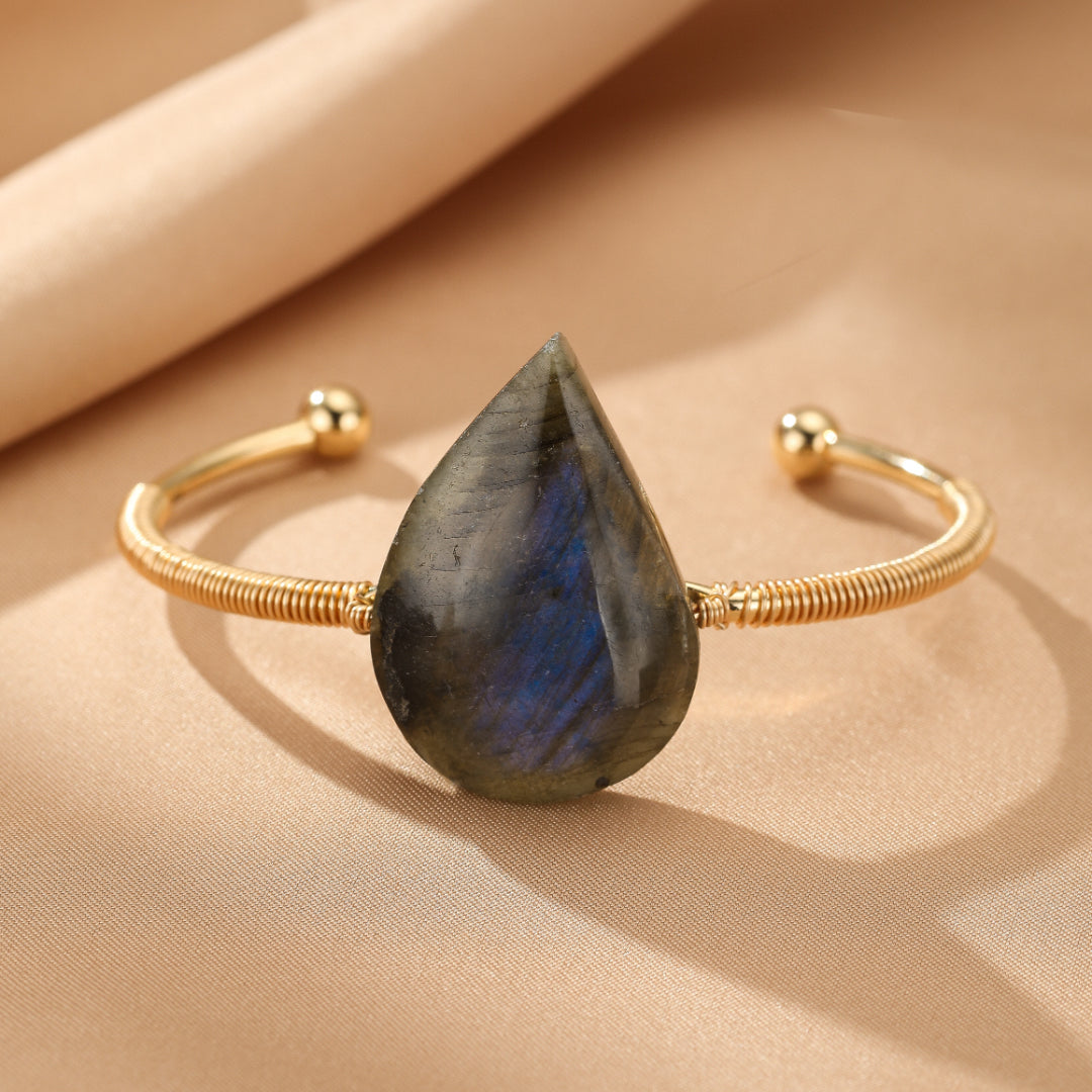 Bracelet jonc plaqué or avec une grosse pierre de labradorite en forme de goutte d'eau, aux reflets bleus et gris, élégant et protecteur.