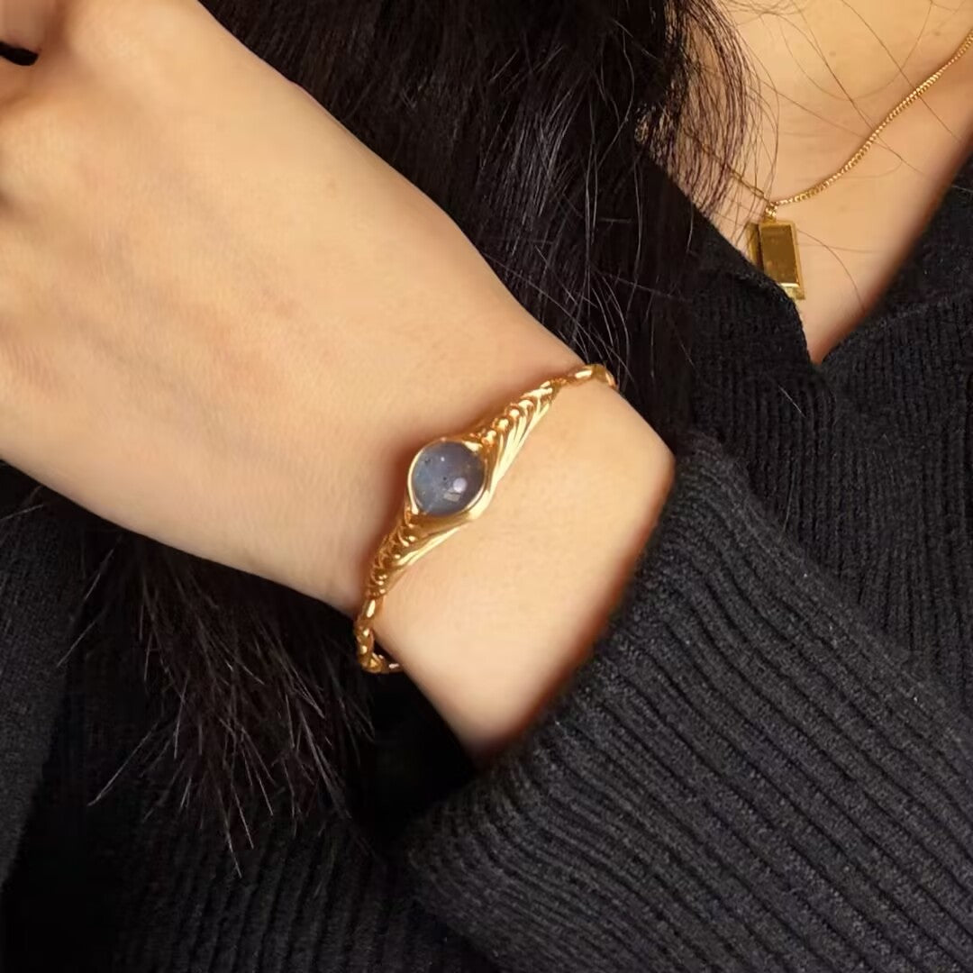 Bracelet doré avec une pierre de labradorite bleue sertie en forme d'œil, porté au poignet d'une femme
