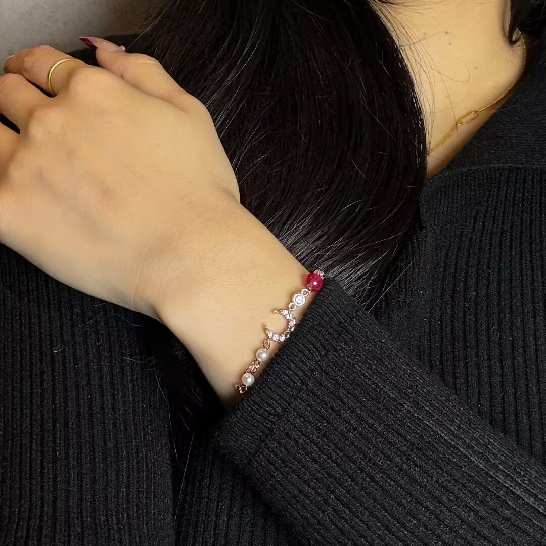 Bracelet délicat en argent avec des perles, une lune sertie de diamants et une pierre rouge, porté au poignet d'une femme.