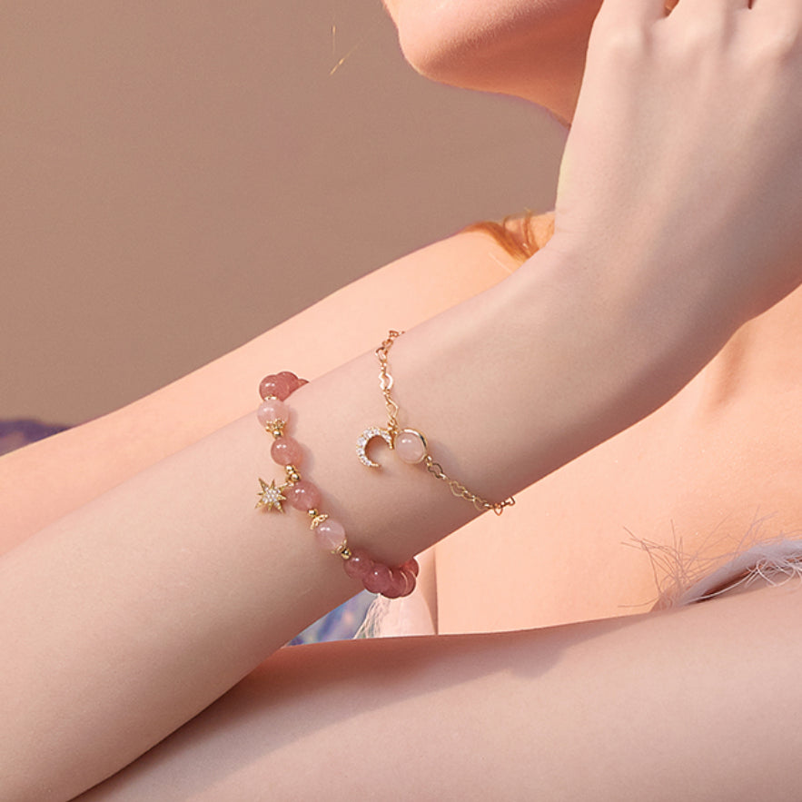 Bracelet en quartz fraise avec pendentifs en forme de lune et d'étoile, porté au poignet d'une femme.