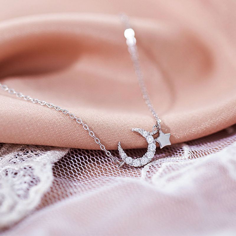 Bracelet délicat en argent avec un pendentif en croissant de lune orné de zircons et une étoile suspendue, sur fond rose et blanc.