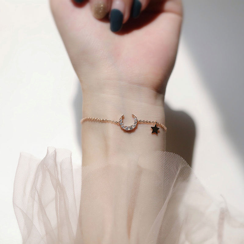 Bracelet fin en argent avec un pendentif en forme de croissant de lune serti de petites pierres scintillantes et une étoile noire suspendue.