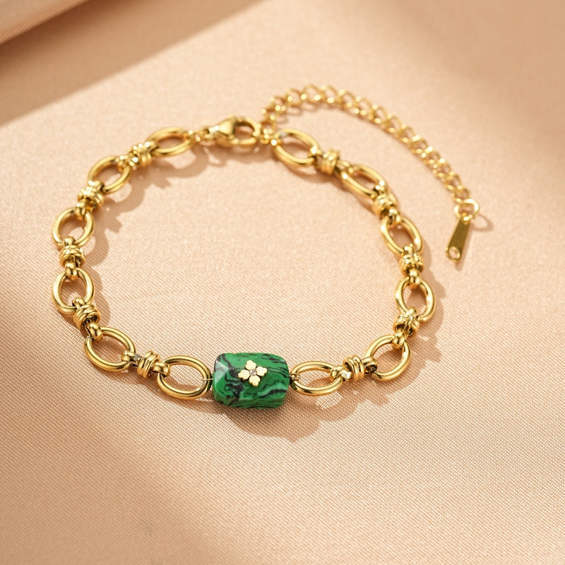 Bracelet en plaqué or avec une pierre centrale rectangulaire en malachite verte veinée et une petite fleur blanche incrustée, maillons ovales entrelacés.