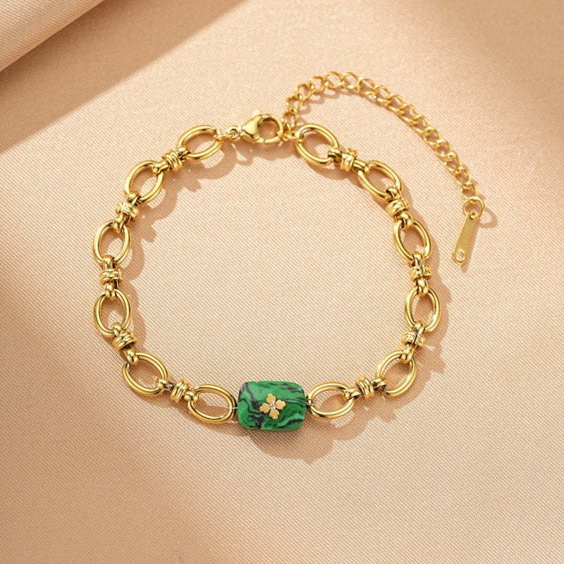 Bracelet en acier inoxydable doré avec une pierre rectangulaire en malachite verte ornée d'une petite fleur dorée au centre, maillons ovales entrelacés et chaîne d'extension.