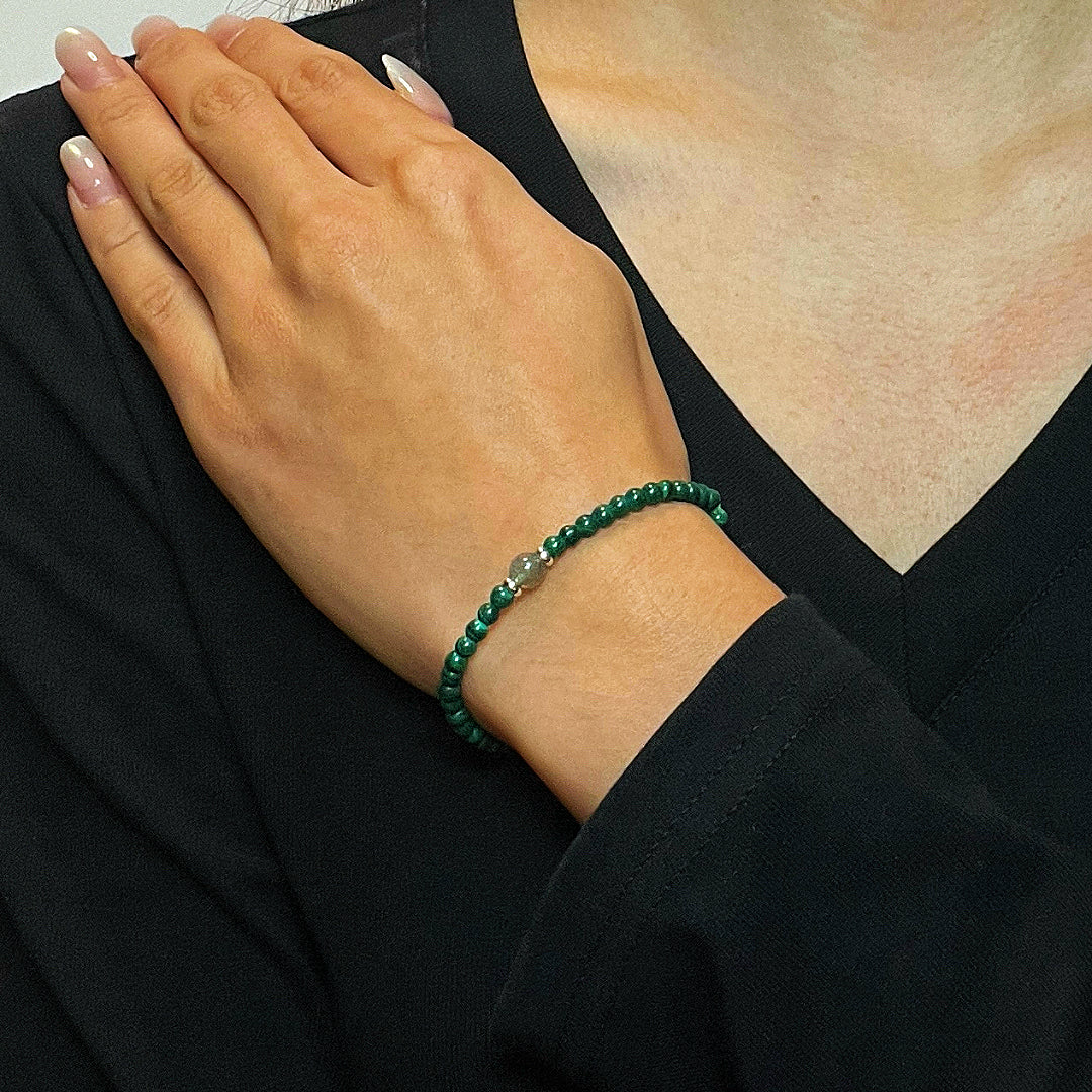 Bracelet fin en malachite avec une perle centrale en argent, porté au poignet d'une femme.